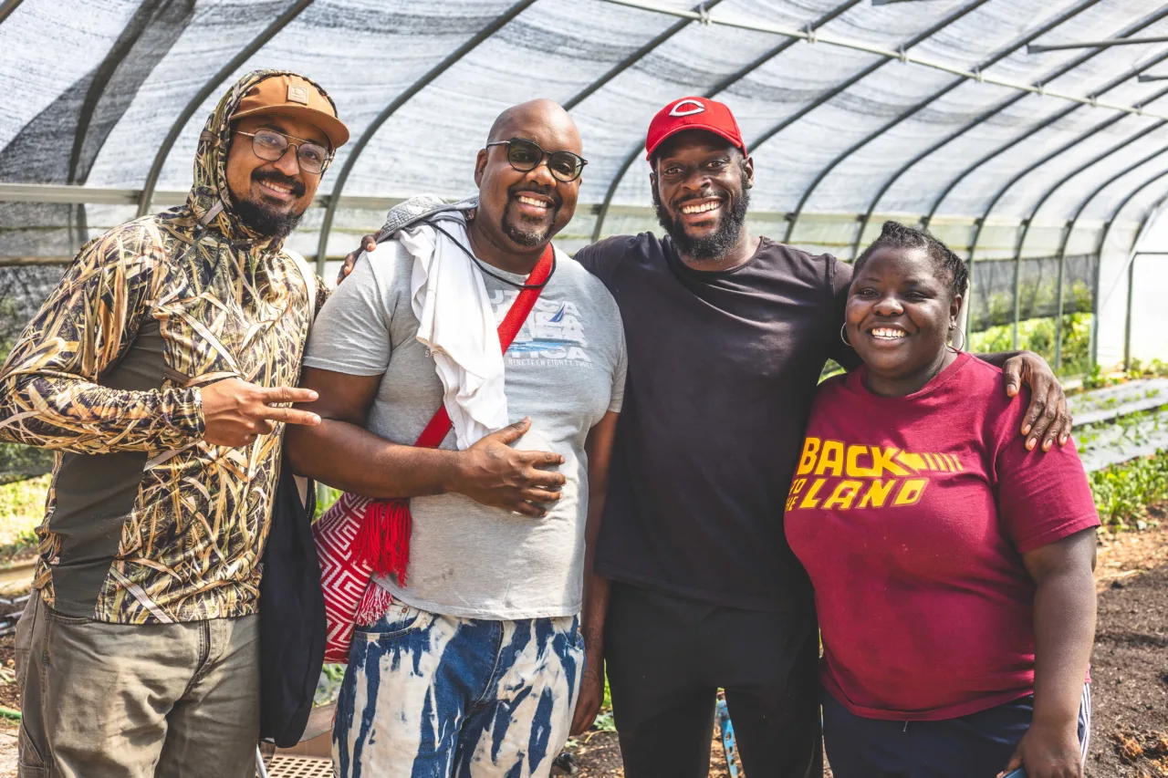 Four people standing outdoors shoulder to shoulder smiling at the camera.